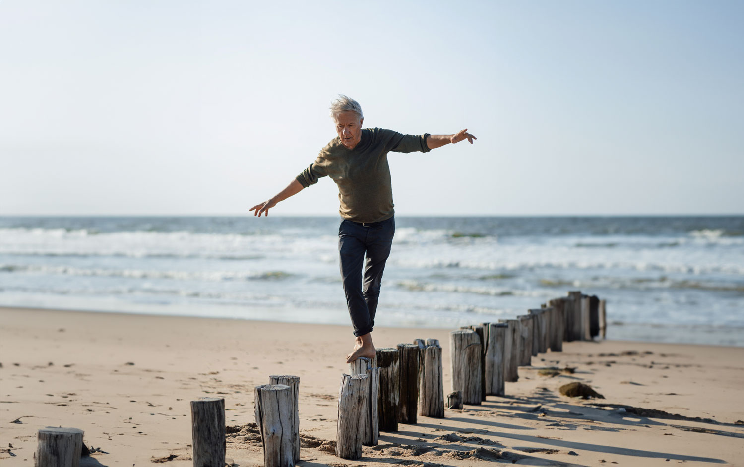 Carefree senior man balancing on wooden posts at beach Recovered